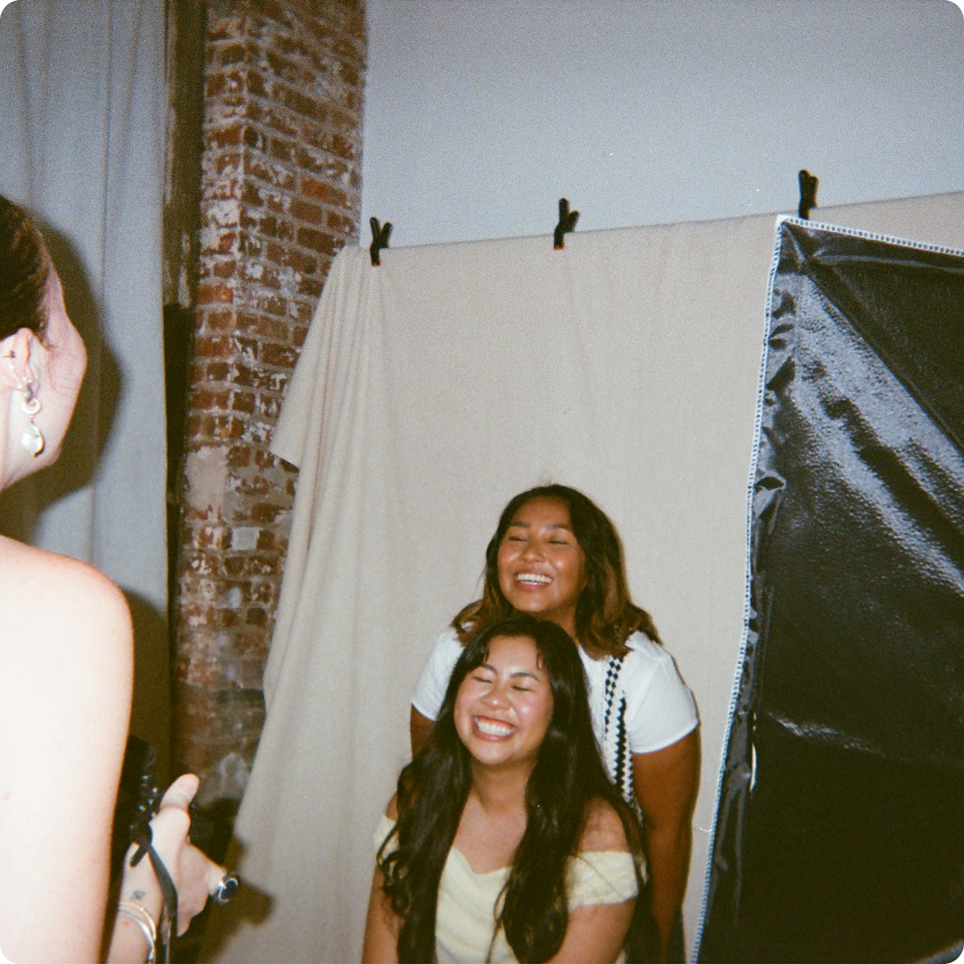 Two women smiling in a photo booth with a brick wall background